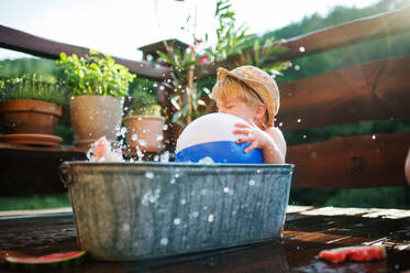 Glücklicher kleiner Junge mit einem Ball in der Badewanne im Freien im Garten im Sommer, spielen im Wasser. - HPIF26364