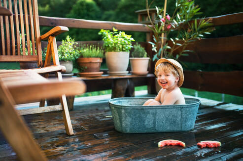 Glücklicher kleiner Junge mit Hut in der Badewanne und Wassermelone im Freien im Garten im Sommer. - HPIF26369
