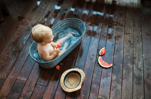 Ein Blick von oben auf glückliche kleine Mädchen in der Badewanne im Freien im Garten im Sommer, Essen Wassermelone. - HPIF26375