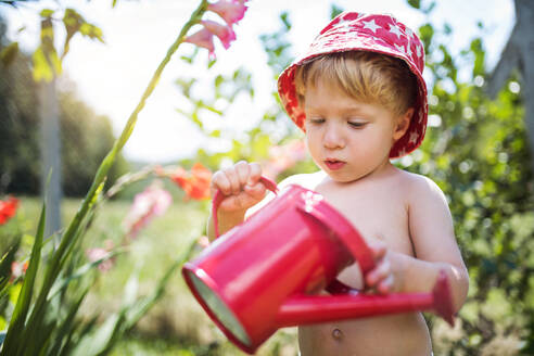 Unbekannter kleiner Junge mit Gießkanne im Garten im Sommer, Blumen gießen. - HPIF26380