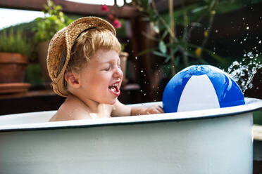 Glücklicher kleiner Junge mit einem Ball in der Badewanne im Freien im Garten im Sommer, spielen im Wasser. - HPIF26394