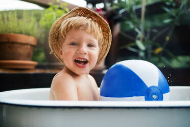 Glücklicher kleiner Junge mit einem Ball in der Badewanne im Freien im Garten im Sommer, spielen im Wasser. - HPIF26397