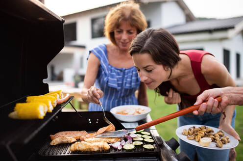 Porträt einer Mehrgenerationen-Familie, die im Garten grillt und sich unterhält. - HPIF26463