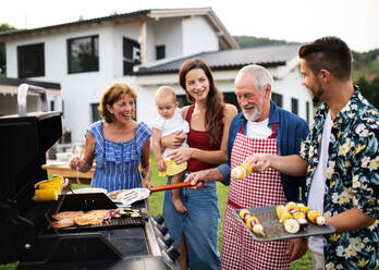 Portrait of multigeneration family outdoors on garden barbecue, grilling and talking. - HPIF26467