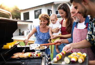 Porträt einer Mehrgenerationen-Familie, die im Garten grillt und sich unterhält. - HPIF26468