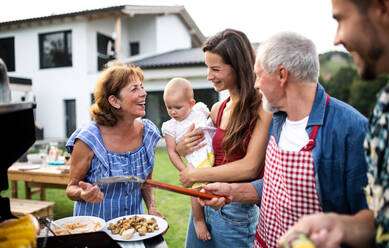 Porträt einer Mehrgenerationen-Familie, die im Garten grillt und sich unterhält. - HPIF26469