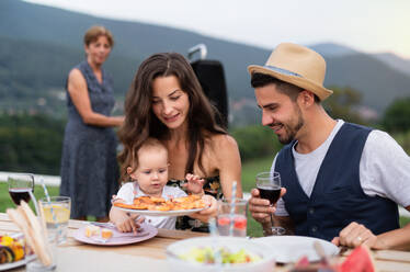 Porträt einer Familie, die an einem Tisch im Freien am Grill sitzt, isst und Wein trinkt. - HPIF26477