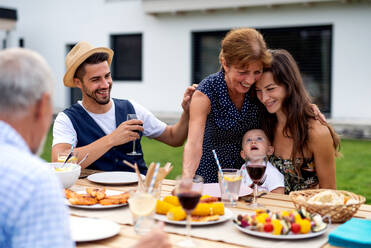 Porträt einer Mehrgenerationenfamilie, die an einem Tisch im Freien sitzt und isst. - HPIF26478