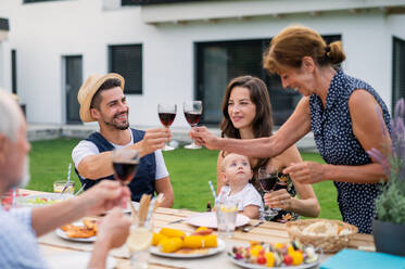 Portrait of family sitting at table outdoors on garden barbecue, eating and drinking wine. - HPIF26479