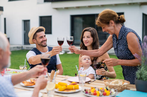 Porträt einer Familie, die an einem Tisch im Freien am Grill sitzt, isst und Wein trinkt. - HPIF26479