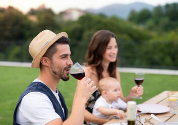 Junges Paar mit Baby sitzt am Tisch im Freien auf Familiengarten Grill, trinken Wein. - HPIF26481