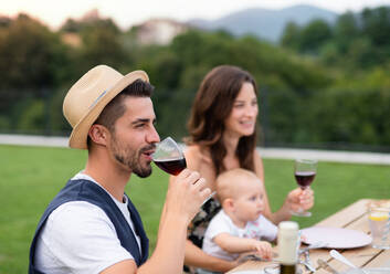 Young couple with baby sitting at table outdoors on family garden barbecue, drinking wine. - HPIF26481