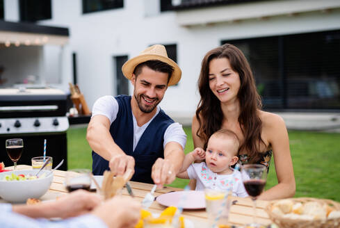 Junges Paar mit Baby sitzt am Tisch im Freien auf Familiengarten Grill, Essen. - HPIF26482