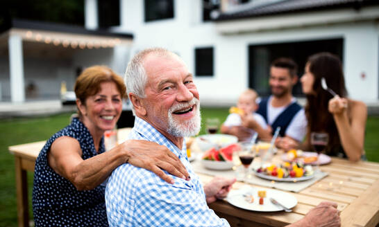 Porträt einer Mehrgenerationenfamilie, die an einem Tisch im Freien sitzt und isst. - HPIF26488