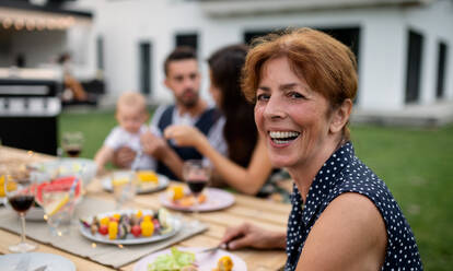 Porträt einer Familie, die an einem Tisch im Freien am Grill sitzt und isst. - HPIF26489