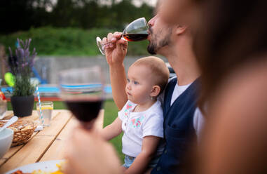 Ein junges Paar mit Baby sitzt am Tisch im Freien auf einer Familienfeier und trinkt Wein. - HPIF26491