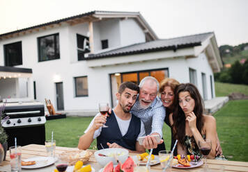 Familie und Freunde genießen ein Barbecue im Garten und halten die Erinnerungen mit einem Gruppen-Selfie auf ihren Smartphones fest - HPIF26494
