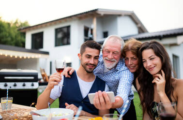 Eine Gruppe von Menschen genießt ein Barbecue im Garten einer Familie und hält den Moment mit einem Selfie auf ihrem Smartphone fest - HPIF26495