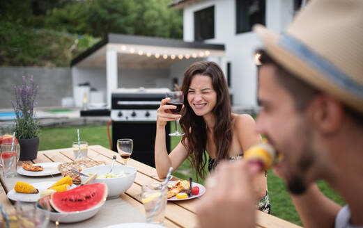 Porträt einer Familie, die an einem Tisch im Freien am Grill sitzt, isst und Wein trinkt. - HPIF26497