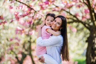 Eine junge Mutter hält ihre kleine Tochter draußen in der Natur im Frühling. - HPIF26506