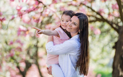 Eine junge Mutter hält ihre kleine Tochter draußen in der Natur im Frühling. - HPIF26507