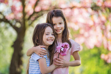Zwei kleine Mädchen stehen draußen in der frühlingshaften Natur und umarmen sich. Raum kopieren. - HPIF26510