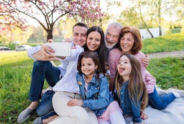 Eine Familie aus drei Generationen macht ein Selfie inmitten der frühlingshaften Natur und benutzt dabei ihre Smartphones - HPIF26554