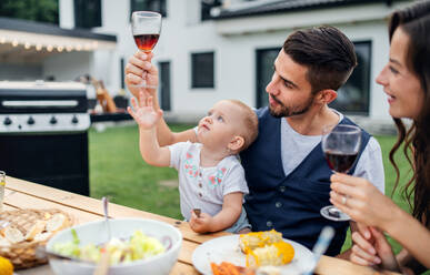 Junges Paar mit Baby sitzt am Tisch im Freien auf Familiengarten Grill, trinken Wein. - HPIF26576