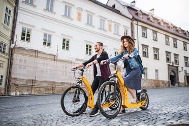 Junges Touristenpaar reist mit Elektrorollern in einer kleinen Stadt, Besichtigung. - HPIF26583