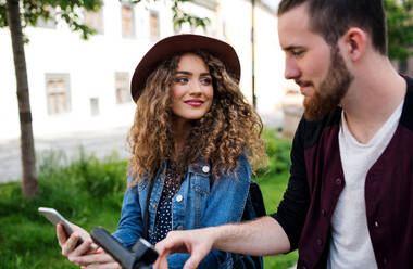 Young tourist couple travellers with smartphone and electric scooters in small town, sightseeing. - HPIF26604