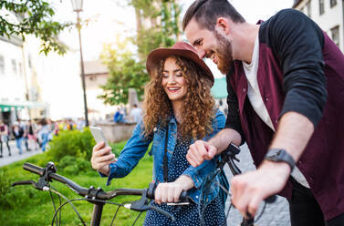 Young tourist couple travellers with electric scooters and smartphone in town, taking selfie. - HPIF26606