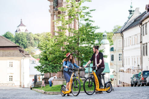 Junges Touristenpaar, das mit einem Elektroroller in einer Kleinstadt unterwegs ist und sich unterhält. - HPIF26607