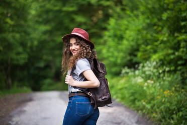 Rückansicht einer jungen Touristin mit Rucksack, die in der Natur spazieren geht, mit Blick zurück. - HPIF26611