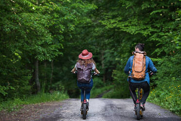 Rear view of young tourist couple travellers with backpacks and electric scooters in nature. - HPIF26621