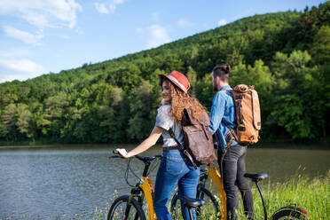 Junges Touristenpaar reist mit Elektrorollern in der Natur, stehend am See. - HPIF26634