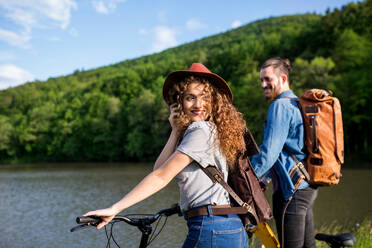 Junges Touristenpaar reist mit Elektrorollern in der Natur, stehend am See. - HPIF26635