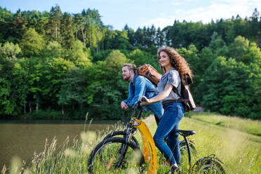 Junges Touristenpaar reist mit Elektrorollern in der Natur, stehend am See. - HPIF26636