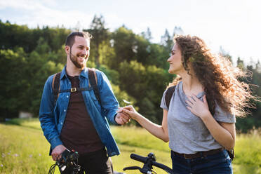 Young tourist couple travellers with backpacks and electric scooters in nature, resting. - HPIF26641