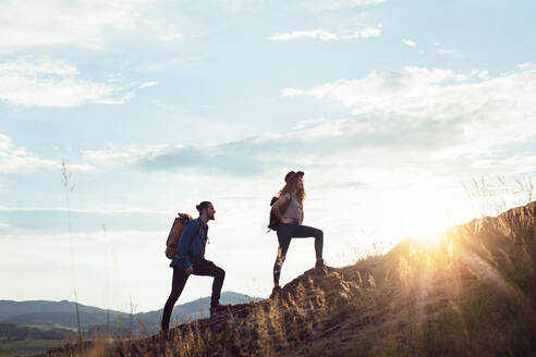 Junges Touristenpaar, das mit Rucksäcken in der Natur bei Sonnenuntergang wandert. - HPIF26647
