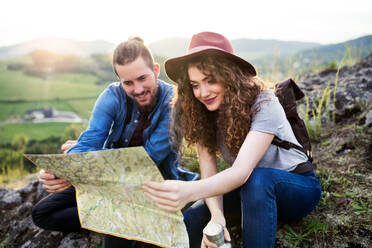 A young tourist couple travellers with backpacks hiking in nature, using map. - HPIF26652