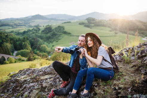 Junges Touristenpaar mit Fernglas beim Wandern in der Natur, sitzend und rastend. - HPIF26655