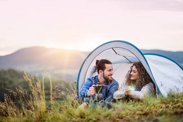 Ein junges Touristenpaar mit Zeltunterkunft sitzt in der Natur und trinkt Kaffee. - HPIF26661