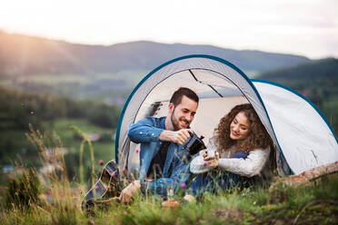 Ein junges Touristenpaar mit Zeltunterkunft sitzt in der Natur und trinkt Kaffee. - HPIF26662