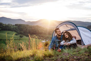 A young tourist couple travellers with tent shelter sitting in nature, drinking coffee. - HPIF26663