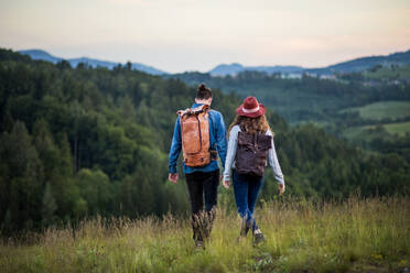 Rückansicht eines jungen Touristenpaares, das mit Rucksäcken in der Natur bei Sonnenuntergang wandert. - HPIF26687