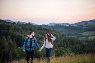 Young tourist couple travellers with backpacks hiking in nature at dusk, holding hands. - HPIF26689