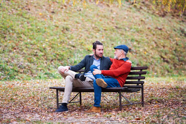 Ein älterer Vater und sein kleiner Sohn sitzen auf einer Bank in der Natur und unterhalten sich. - HPIF26691