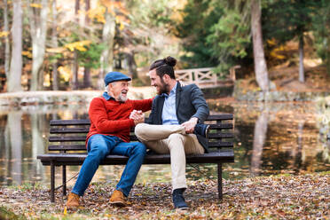 Senior father and his young son sitting on bench by lake in nature, talking. - HPIF26696