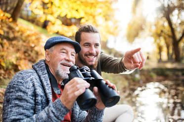 Senior father and his son with binoculars sitting on bench in nature, talking. - HPIF26706