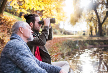 Senior father and his son with binoculars sitting on bench in nature, talking. - HPIF26707